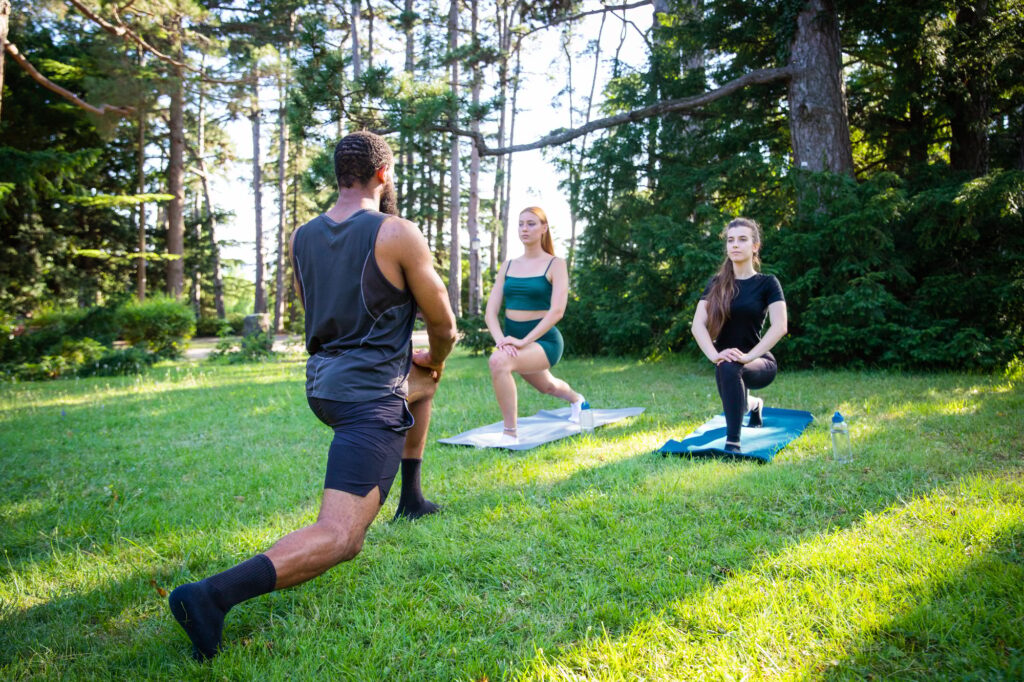 A fitness coach holds a class with two girls and they perform exercises in a public park